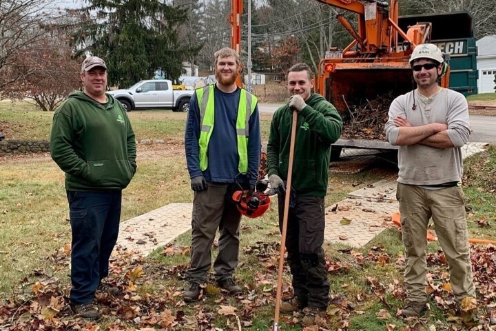 Group of Tree Tech arborists posing for a photo around raked leaves and a wood chipper